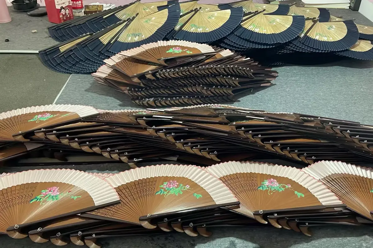 Batches of floral folding fans arranged open and partly folded on a worktable.