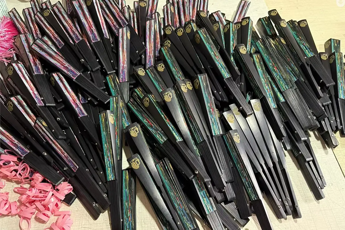 Folded fans with black guards and colorful printed leaves arranged in batches.