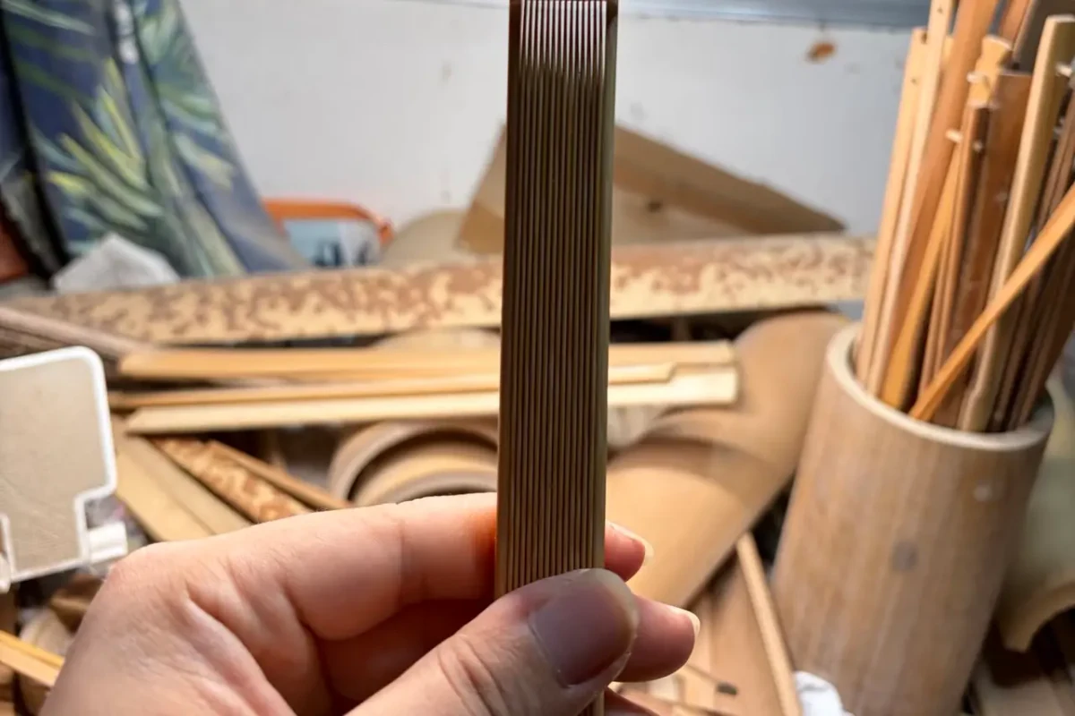 A folded fan frame held upright above a workbench, with the stacked ribs visible.