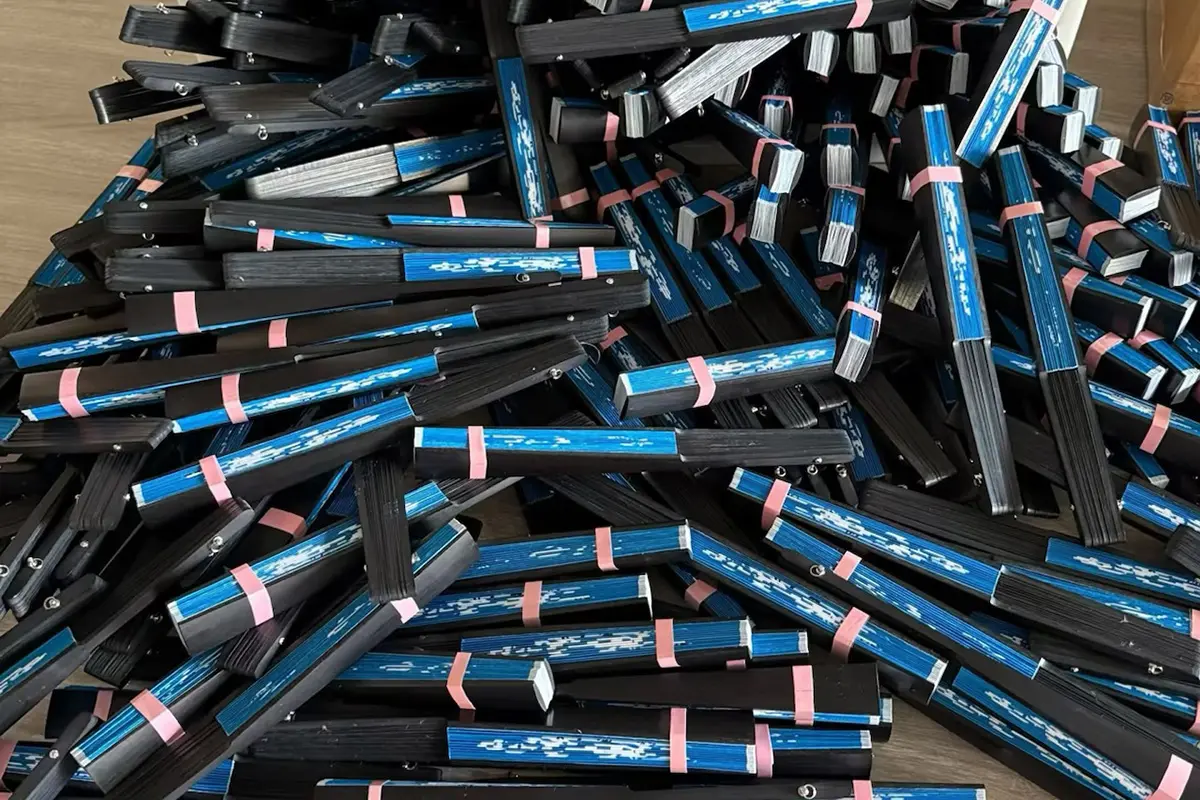 A batch of folded blue-print fans with black guards and pink bands.