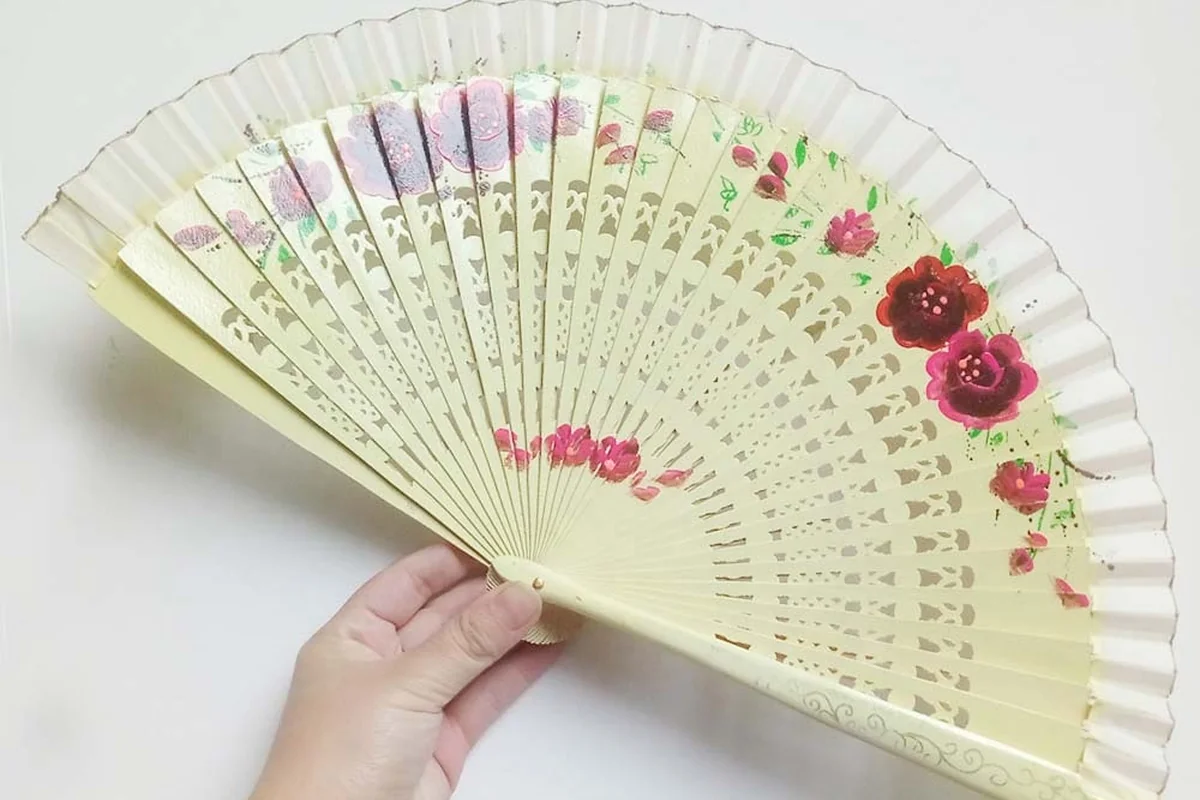 Pale pierced folding fan with a small floral design held open in one hand.