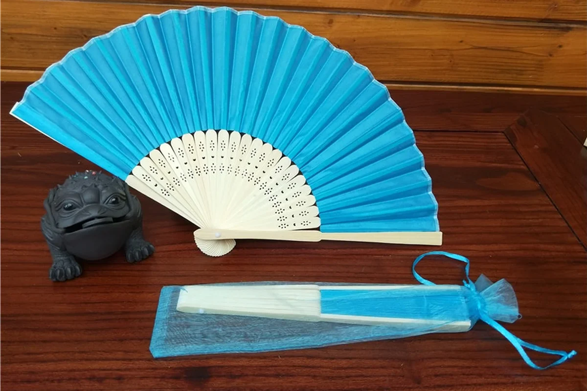 Blue folding fan with a matching drawstring pouch on a wooden surface.