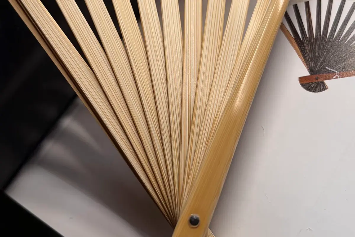 An open natural-colored fan frame showing the ribs, outer guard and pivot.