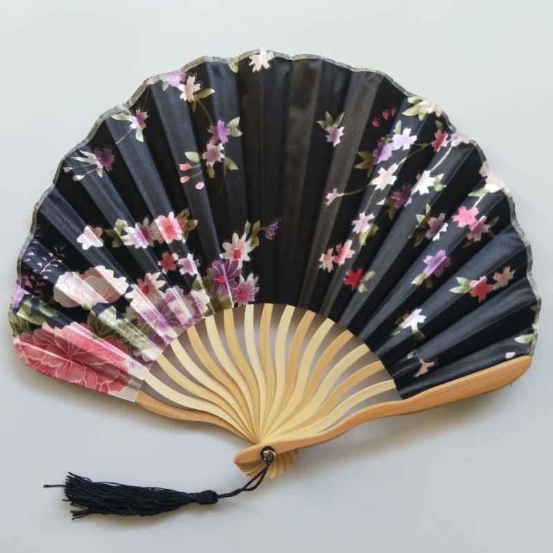 Black blossom folding fan photographed at an angle with its tassel