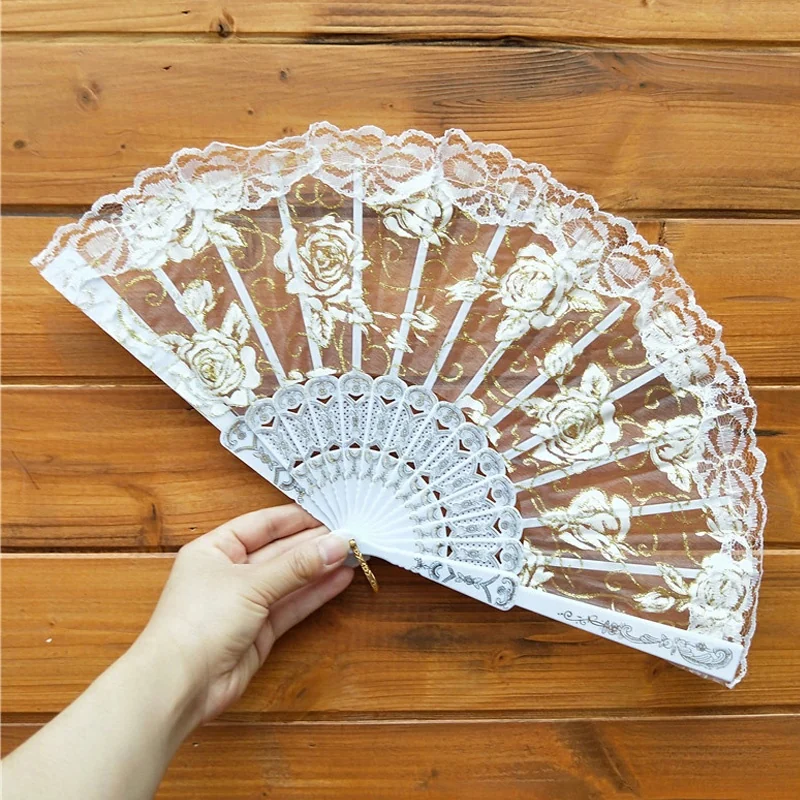 White floral lace folding fan held open against a wood background