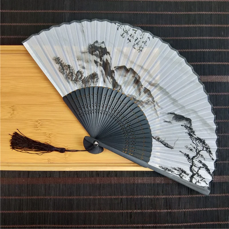 Monochrome landscape folding fan with black ribs and tassel on a tray