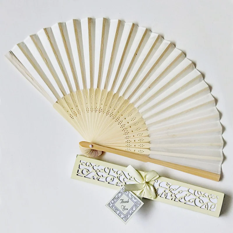 Ivory folding fan beside a decorative favor box with ribbon and tag