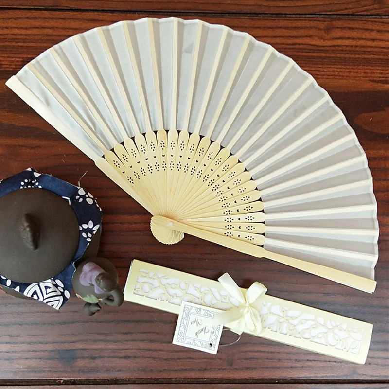 Ivory wedding fan and ribboned box displayed on a wooden surface