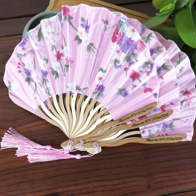 Several pink floral wedding fans arranged to show their handles and printed leaves