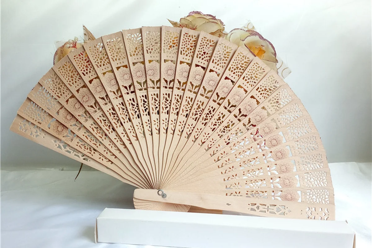 Pale folding fan with intricate cutout patterns on a white display stand.