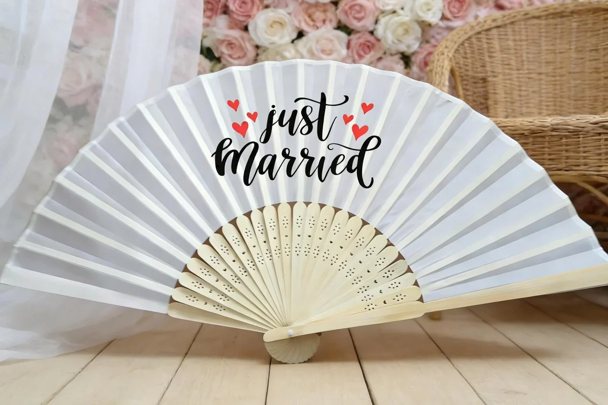 White Just Married folding fan beside flowers.