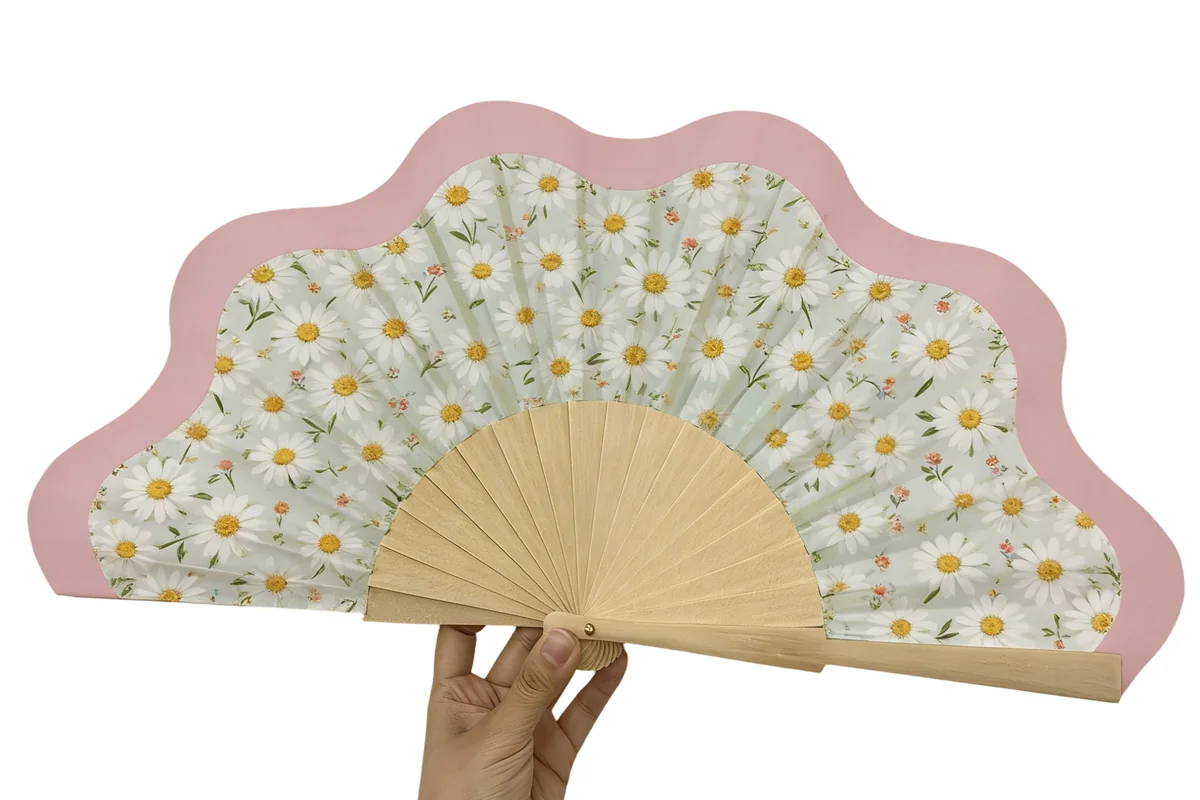 Scalloped folding fan with a pink border and white daisies, held in one hand.